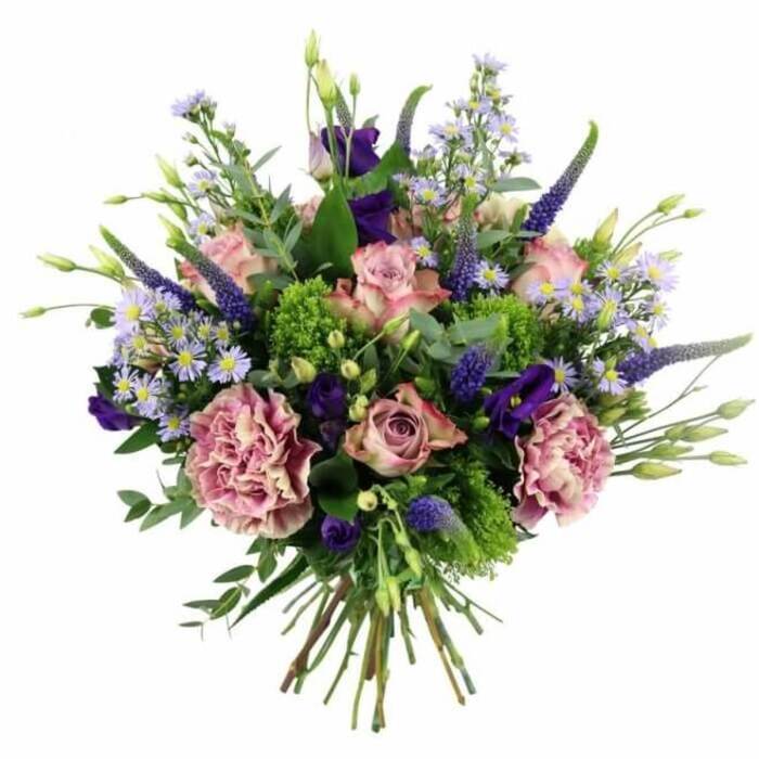 This image shows a meticulously crafted hand-tied bouquet resting against a white studio-style background, allowing every flower and leaf to stand out with clarity, as if it had just been prepared in a Wapping florist's workshop near the historic wharves. The composition is generously rounded and full, overflowing with a harmonious blend of pinks, mauves, purples, and vivid greens. At the centre and scattered throughout, soft pink roses unfurl layer by layer, some blossoms fully open and others half-closed, with petals that deepen in colour toward the core and then fade to delicate blush and near-cream at the tips. These romantic blooms are closely accompanied by large, frilled carnations in dusty rose and purple-mauve shades, their many ruffles catching shadows and light to build depth and texture. Rising above and threading between the rounder blossoms, slender Veronica spikes in deep lavender-blue stretch upward, lending a sense of vertical motion and garden-like elegance. Surrounding them are airy clusters of dainty, aster-like flowers in light lilac and periwinkle, each with a tiny yellow centre that brightens the palette and fills the gaps with soft, clouded colour. Tucked among the petals, darker purple lisianthus add a quiet richness, like little pockets of twilight. The whole design is framed and anchored by varied foliage: broad, silvery eucalyptus leaves curl gently at the edges, while bright lime and chartreuse green fillers provide a lively contrast, reminiscent of the fresh greenery in nearby Wapping Woods. The stems are gathered neatly at the base in a classic hand-tied style, ready to be placed straight into a favourite vase after local delivery. This bouquet evokes sophistication and tenderness, well suited for birthdays, anniversaries, or any heartfelt gesture shared between neighbours along the Thames.
