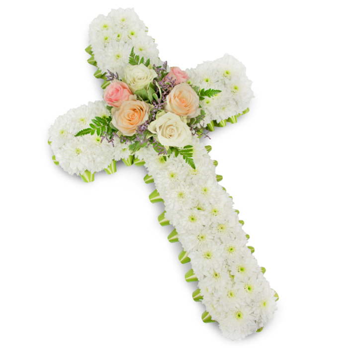 A beautifully composed floral cross, designed as a funeral tribute, stands out clearly against a bright white background, reminiscent of a display you might see at a quiet memorial service in Wapping or along the Thames path. The cross is built with a generous, solid frame and completely paved in delicate white button chrysanthemums, their small, round heads packed shoulder to shoulder to form an unbroken carpet of petals. This dense layer of snowy blooms gives the piece a soft, cushioned look, evoking purity, reverence, and a sense of gentle protection around the memory of a loved one. At the heart of the cross, where the vertical stem and arms intersect, sits a thoughtfully arranged posy of roses. Several fully open roses in creamy ivory, tender blush pink, and warm peach tones are arranged so their spiralling centres are clearly visible, surrounded by airy green fern fronds and fine stems of light purple or lavender filler flowers. This central cluster forms a natural focal point, suggesting love, gratitude, and cherished moments shared. Tracing the entire perimeter of the cross is a narrow band of lime green ribbon, tucked just beneath the chrysanthemums so that a crisp outline of colour frames the white blooms. The ribbon's fresh green hue provides gentle contrast without overpowering the peaceful palette. The lighting in the image is clean and even, enhancing every texture and hue. This floral cross would be an especially meaningful tribute for funerals and memorials held in Wapping, bringing a sense of quiet dignity and spiritual comfort to the occasion.