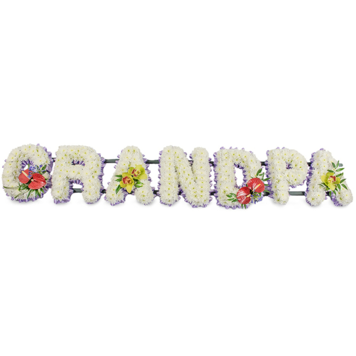 Set against a plain white backdrop, this long, carefully constructed floral display spells out "GRANDPA" in sturdy capital letters, designed as a prominent tribute for a funeral or celebration of life. Each letter is built up from a mass of small, uniform white chrysanthemums, their rounded petals tightly overlapping so that no gaps in the base are visible. The result is a plush, pillowed effect, as though each letter were softly upholstered in flowers, symbolising comfort, purity, and a peaceful farewell. Around the base of the letters, a band of pale lilac ribbon peeks out, encircling the arrangement with a cool, calming hint of colour and neatly finishing the edges. Hidden dark green supports run horizontally behind the flowers, linking the letters together and ensuring the tribute can be safely displayed at a service in Wapping, perhaps in a riverside chapel or community hall off Wapping High Street. The visual rhythm of the white lettering is thoughtfully broken up by four vivid accent sprays. On the "G" and the "D", clusters of deep red anthuriums draw the eye, their sculptural, heart-shaped spathes and central spadices rising above polished green foliage like small, shining emblems of love and courage. On the first "A" and the last "A", graceful yellow-green orchids are nestled among fresh greenery, their luminous lime tones and fine, arching petals suggesting remembrance, admiration, and the quiet continuation of family stories. Crafted with the sensitivity of an experienced local florist, this "GRANDPA" tribute feels both grand and gentle, an eloquent way for families in Wapping to honour a cherished grandfather's life, character, and legacy.